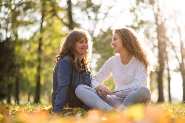 Mom and daughter sitting outside in sunlight in conversation. 